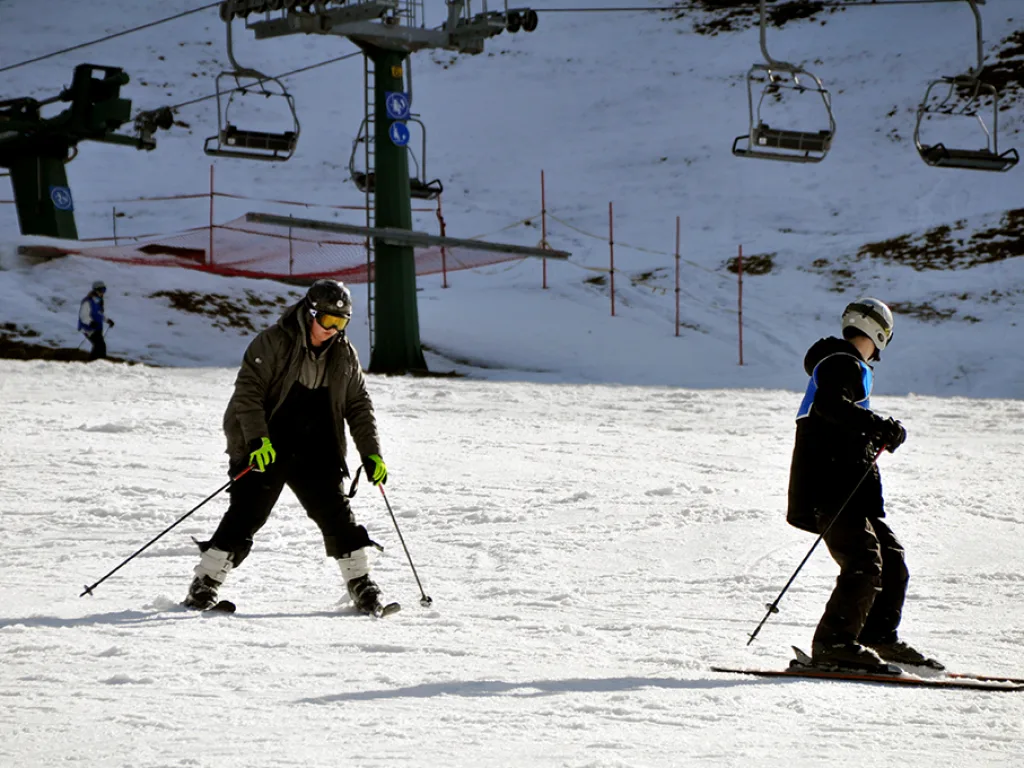Zwei Skifahrende auf der Piste unter dem Sessellift.
